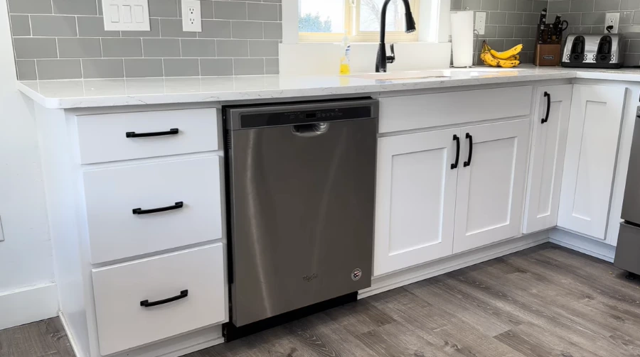 Stainless steel Whirlpool dishwasher installed in a white shaker-style kitchen